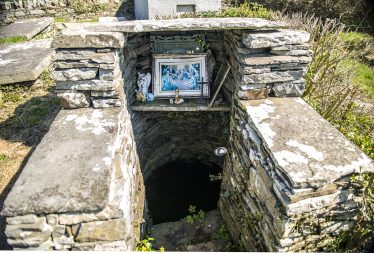 Saint Senan's Well, Tullaher, Well made from light grey stone in foreground, with religious image in frame at back of well | James Feeney